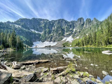 Reflective lake with pine trees, rocky shore, and mountain